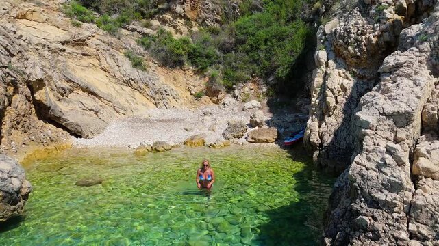 Beautiful Young Woman in Bikini Swims in Stara Baska Beach Krk Island, Croatia. Mediterranean Summer. Aerial Shot From Above. Blue Sea the Rocks Mountains and Coastline Calm Sea With Clear Blue Water