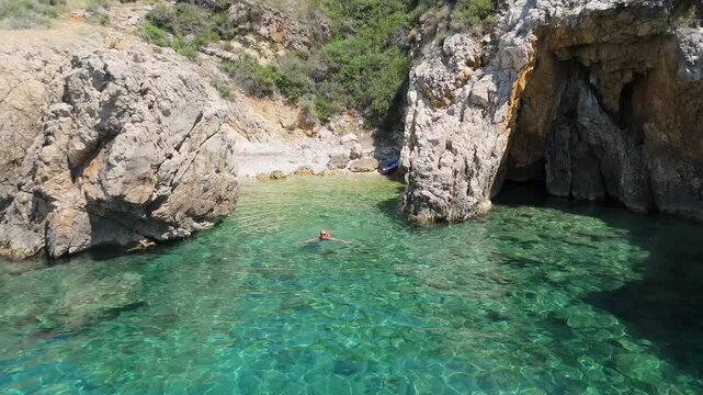 Beautiful Young Woman Naturalist Swims in Stara Baska Beach Krk Island Croatia. Mediterranean Summer. Aerial Shot From Above. Blue Sea the Rocks Mountains and Coastline Calm Sea With Clear Blue Water