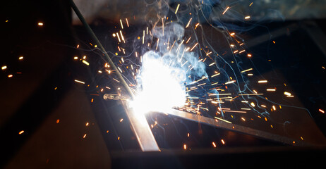 A welder is working on a piece of metal, creating sparks and smoke