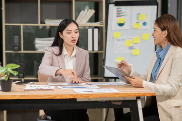 Two businesswomen using laptops and graph paper discuss and consult with each other.