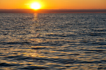 The sun is setting over the ocean, casting a warm glow on the water
