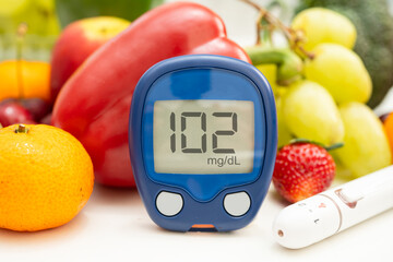 Asian hand holding digital glucose monitor measure with vegetable and fruit healthy food.