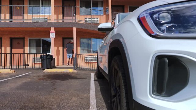 A man walks towards a specific hotel room after getting out of a parked car located in the motel lot, effectively showcasing themes of travel, leisure, and accommodation throughout his journey
