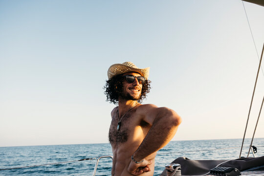 Carefree man wearing straw hat and sunglasses enjoying summer vacations sailing in the ocean - Powered by Adobe
