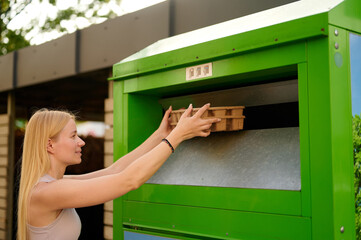 woman recycling cardboard at green recycling bin outdoors. environmental awareness and...