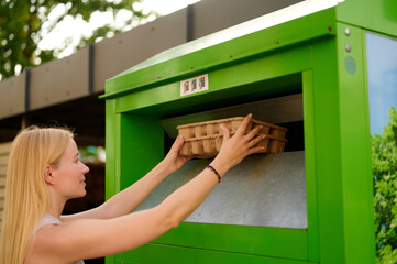 woman recycling cardboard at green bin station outdoors, engaging in sustainable waste management. encourages environmental responsibility and illustrates eco-friendly practices and green living.