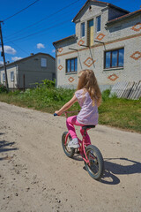little girl riding a bike on a village street, A little girl is on vacation in the village. She...