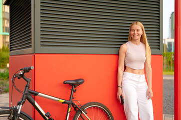 woman standing by urban bike confidently holds smartphone while smiling outdoors. casual modern lifestyle, relaxed atmosphere, cycling culture, youthful street fashion