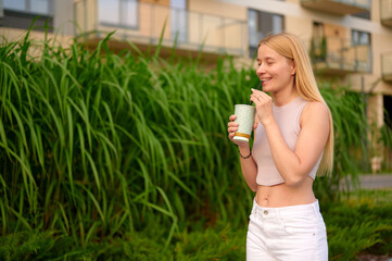 woman enjoying cold drink outdoors near lush greenery. casual summer fashion, carefree relaxation, and refreshing moments in urban setting. perfect for lifestyle and wellness themes