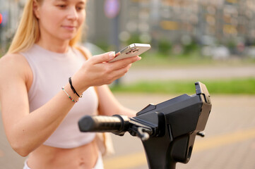 woman using smartphone to unlock electric scooter outdoors. modern urban mobility and sustainable...