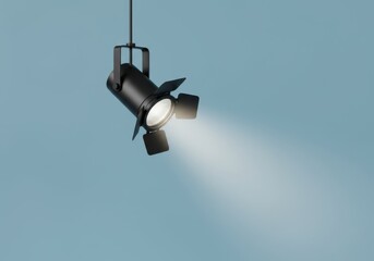 A black spotlight illuminates a clear beam of light against a soft blue background