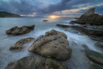 Dramatic seascape at sunset in Azkorri beach, Getxo, Basque Country, with waves flowing between rugged rocks under stormy clouds