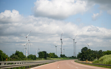 Wind turbines along highway under cloudy sky on summer day, renewable energy landscape