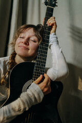Young woman musician playing acoustic guitar at home, eyes closed and fully immersed in the music,...