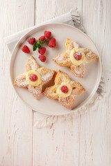 Sweet puff pastry with vanilla custard and fresh raspberries close-up in a plate on the table. Vertical top view from above