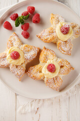 Puff flower-shaped cake with custard cream and fresh raspberries close-up in a plate on the table. Vertical top view from above