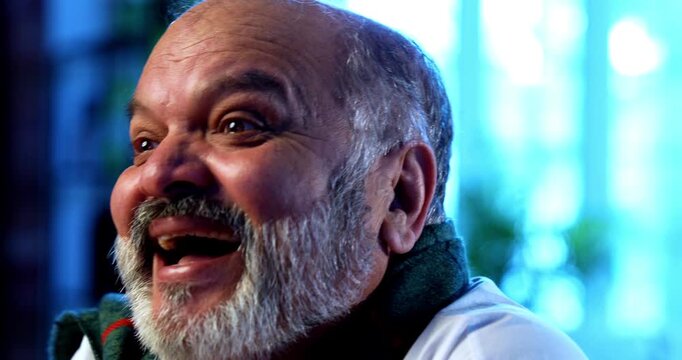 Indian senior man smiling closeup at home at table, cheerful elderly asian male expressing happiness and calmness in retirement, peaceful retired lifestyle, joyful facial expression indoors