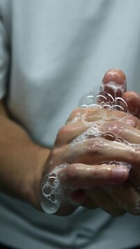 A man in a white T-shirt washes his hands with soap in the bathroom.
Hygiene and hand disinfection with antibacterial soap.
Health and hand hygiene close-up.
Soapy hands