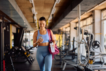 Happy athletic woman using app on smart phone during gym workout.