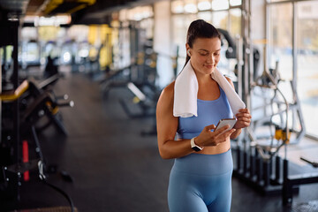 Happy athletic woman texting on cell phone while exercising in gym.