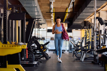 Full length of sportswoman with cell phone walking through health club.