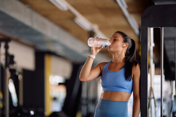 Young athletic woman drinking water during sports training in gym.