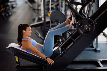 Young sportswoman working out on leg press machine in health club.