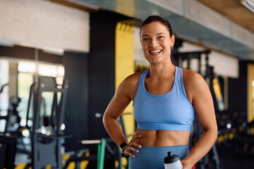 Portrait of happy sportswoman with water bottle in gym looking at camera.