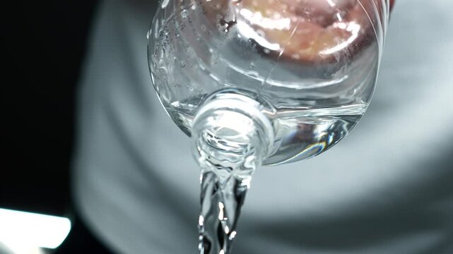 Water pours from a bottle on a white background.
A man in white clothes pours water from a plastic bottle close-up