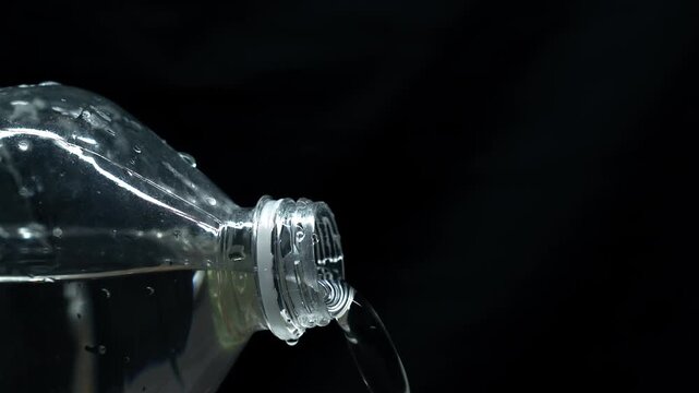 A stream of purified, refreshing water flows out of a plastic bottle.
Transparent container with water on a black background.
Strong water pressure from the bottle.