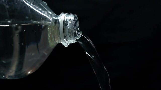 Water flows out from an open plastic bottle on a black background.
A stream of purified water pours down from the container.
Purified drinking water in a bottle on a black isolated background