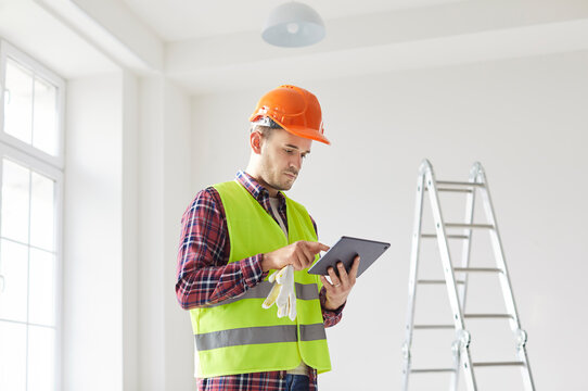 Serious worker or contractor planning a home renovation, reviewing a blueprint and draft on a tablet PC. The project focuses on construction and careful planning for a successful renovation.