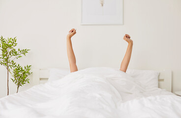 Hands of young woman stretching after waking up. Happy young woman lying in cozy comfortable bed...