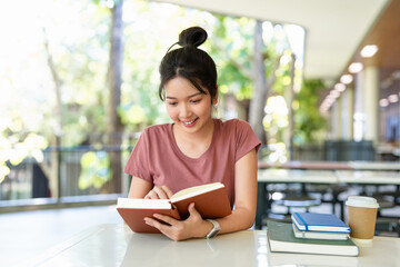 Female student sitting in cafeteria, reading book, studying for final exam at university.