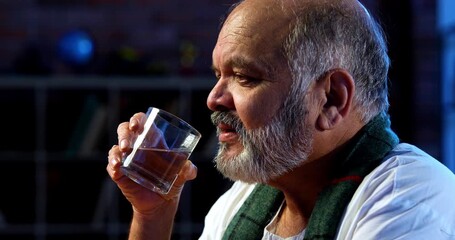 Indian senior man drinking water from glass while sitting at table in modern home, healthy happy old aged asian male staying hydrated indoors in casual wear during relaxing daytime lifestyle routine - Powered by Adobe
