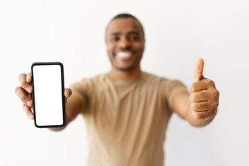 Cheerful black man showing thumb up and holding smartphone with blank screen. Positive, user...