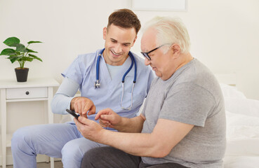 Smiling male doctor or nurse provides guidance to a senior man in using phone, online platforms,...
