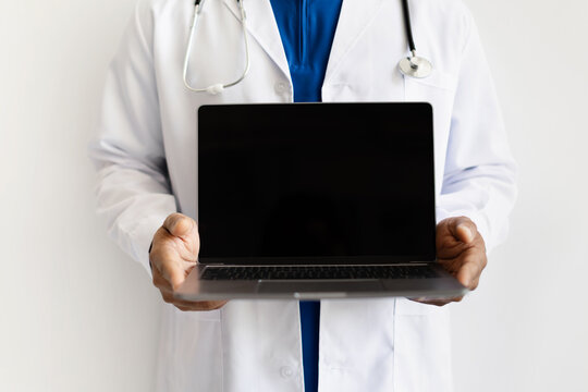 Closeup of African American doctor holding laptop with blank screen. Mockup concept for medical software, online services or digital health platforms