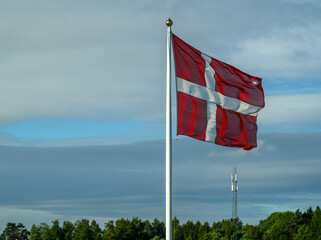 A vibrant Danish flag flies proudly on a flagpole amidst a backdrop of scattered clouds and...