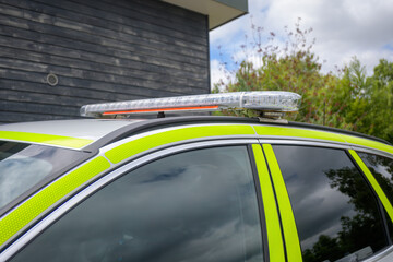 A marked police vehicle is stationed in a lush green environment, displaying its light bar as a sign of readiness for public safety operations. The scene suggests a focus on community vigilance