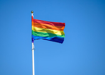 A vibrant rainbow flag flutters in the wind under a bright blue sky. This symbol of pride reflects a commitment to equality and acceptance during a lively community event