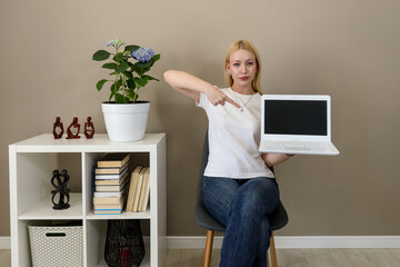 Confident woman pointing at blank laptop screen in home office