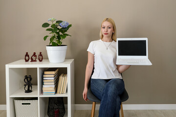 Woman showing blank laptop screen in stylish home setting