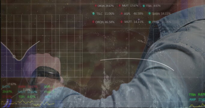 Pointing male in blue shirt exploring stock charts on glass display at modern office, copy space