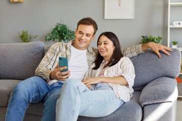 Married couple spending leisure time at home using a phone for online entertainment and...