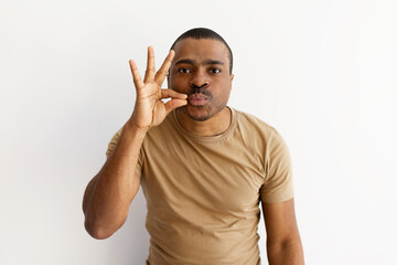 Playful black man gesturing zipped lips with fingers, expressing silence or secrecy. Lighthearted,...