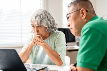 asian senior couple sitting at table at home making financial plan using laptop computer.