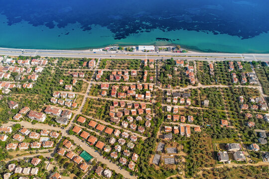 Drone capturing a residential area along the coast, showcasing houses, roads, trees, and the beautiful turquoise waters of mediterranean sea - Powered by Adobe