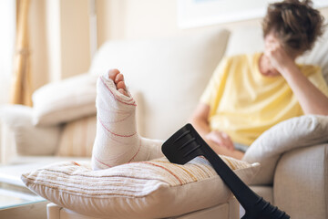 Patient is recovering at home with a broken leg in a cast, resting on a pillow with crutches...