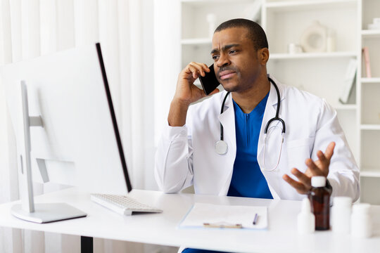 Concerned African American doctor gesturing during phone call at work. Frustrated male physician having difficult discussion, showing emotion and stress in clinic office
